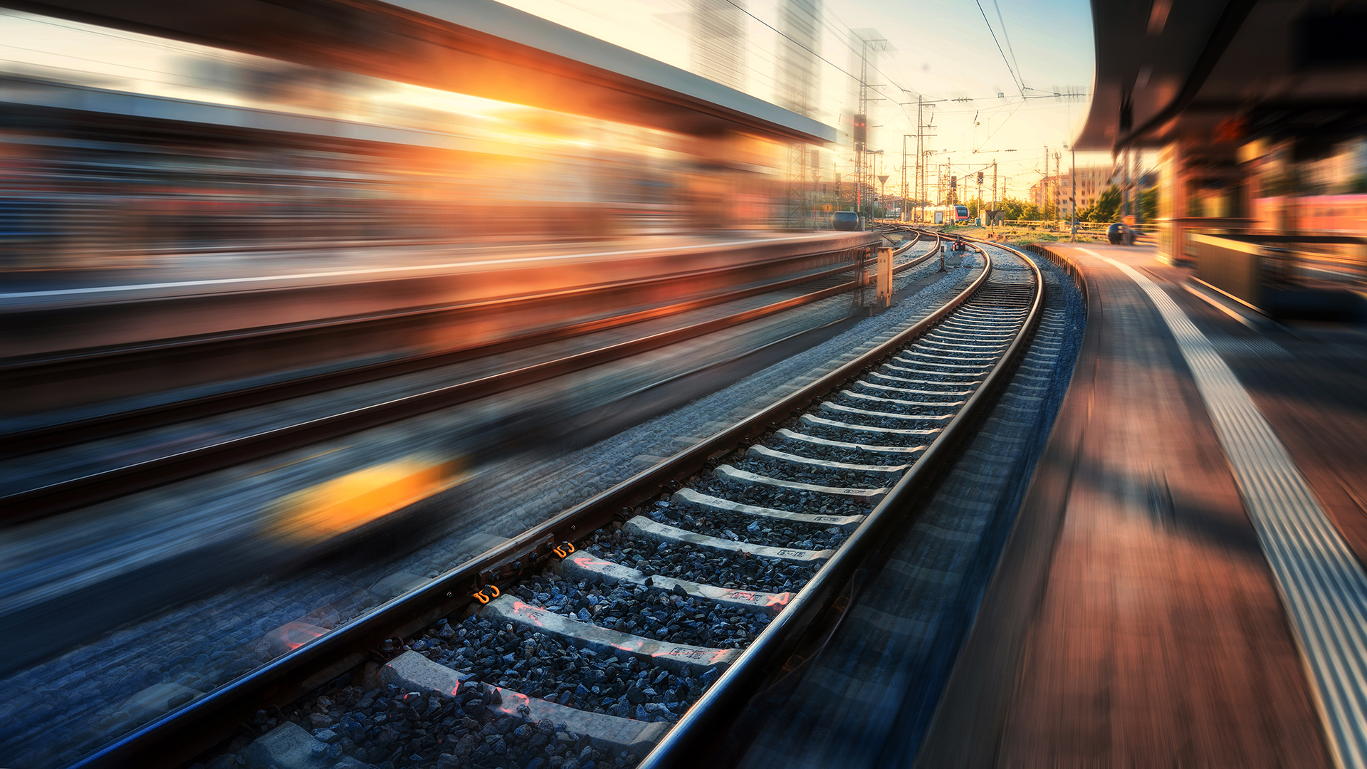 Railway station with motion blur effect at sunset. Industrial landscape with railroad, blurred railway platform, sky with orange sunlight in the evening. Railway junction in Europe. Transportation
